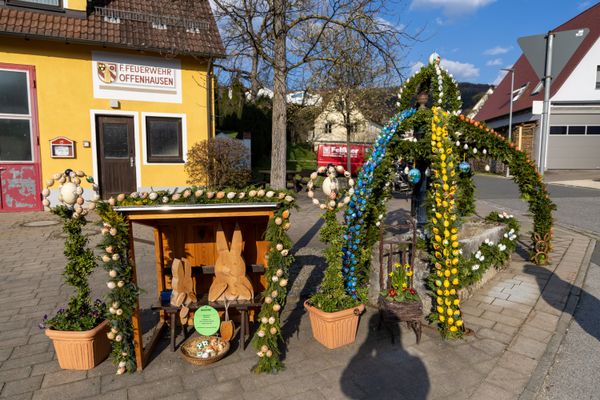 Kleine Osterhütte mit zwei hölzernen Hasen neben Osterbrunnen.