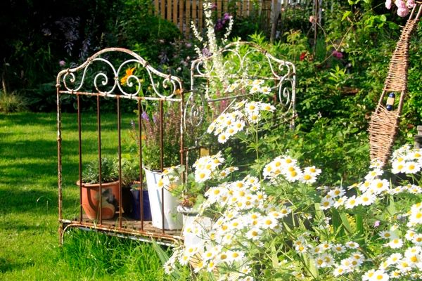 Der Betrachter blickt auf ein dekoriertes Eck im Garten, Im Vordergrund eine Staude.
