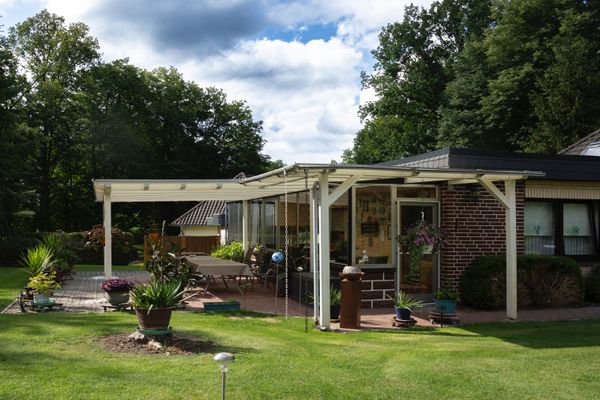 Überdachte Terrasse mit Sitzmöbeln und Topfpflanzen, angrenzend an Rasenfläche und Garten.