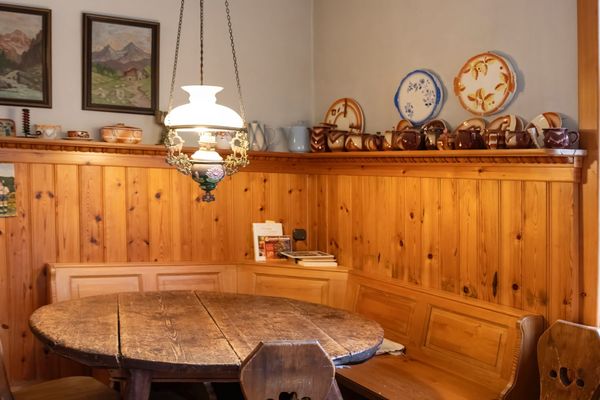 Essbereich mit rundem Holztisch, Sitzbank und Wandregal mit Geschirr unter einer Hängelampe.