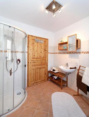 Badezimmer mit Eckdusche, Waschbecken, Spiegel und Handtuchbutler.