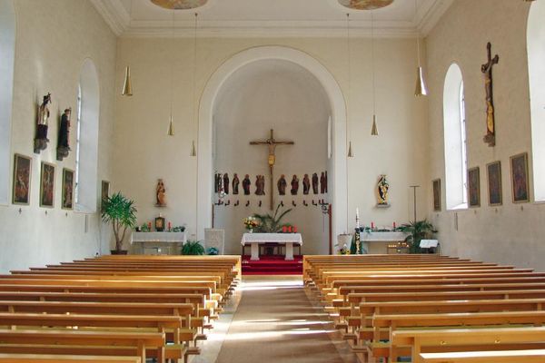 Schlichter Kircheninnenraum mit Hauptaltar, Seitenaltären, mehreren Heiligenfiguren, Kreuzwegstationen, Kruzifix, zwei kleinen Deckengemälden und Bankreihen.