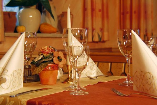 Ein schön gedeckter Tisch mit einer orangefarbigen Tischdecke und einem gelben Tischläufer. Darauf stehen unter anderem vier Weingläser und eine Kerze.