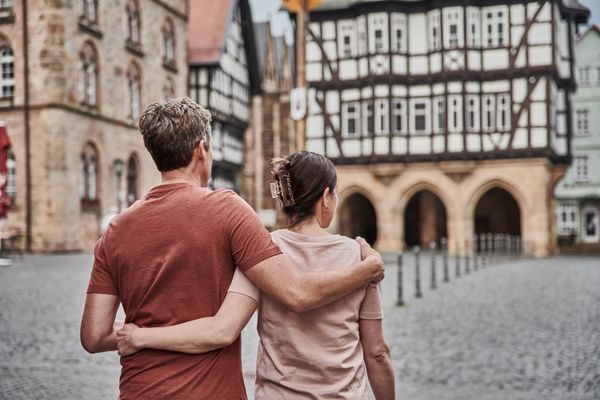 Ein Paar läuft Arm in Arm durch die Fachwerkaltstadt von Alsfeld. Man sieht sie von hinten, vor Ihnen sind historische Fachwerk- und Steinhäuser verschwommen zu sehen.
