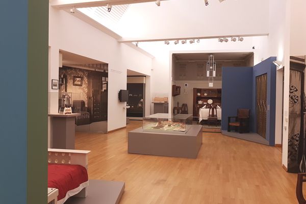 Ausstellungsraum mit historischen Möbeln und Vitrinen auf hellem Holzboden, weiße Wände und Decke mit Oberlicht.