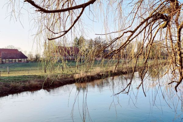 Blick über die Ilmenau bei Klein Bünstorf. Die historische Hofanlage mit Fachwerkhäusern liegt nahe dem Kanuanleger. Die Ilmenau ist hier Teil der Rad- und Kanurouten durch die Heideregion.