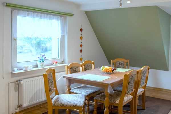 Holztisch mit sechs Stühlen nahe einem Fenster, darauf eine Schale mit Obst