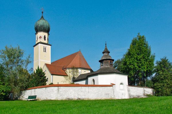 Hinter einer Mauer mit Ziegelabdeckung steht die achteckige Friedhofskapelle Heilig Kreuz in Haselbach. Turm und Kapellendach sind mit Schindeln gedeckt. Hinter der Friedhofskapelle erhebt sich die Pfarrkirche St. Jakob mit Zwiebelturmkuppel.