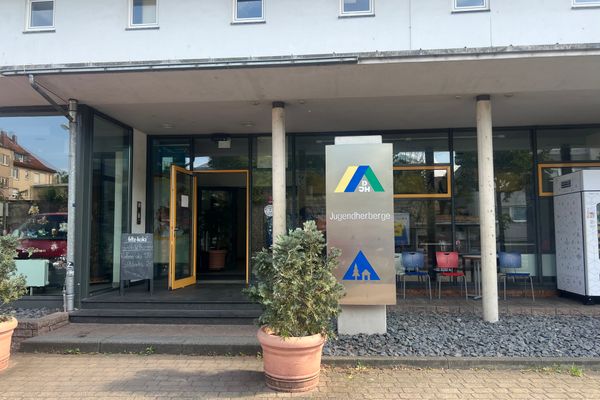 Eingangsbereich einer Jugendherberge mit offenem Glastürrahmen, zwei Säulen und einem Schild mit dem Jugendherbergslogo