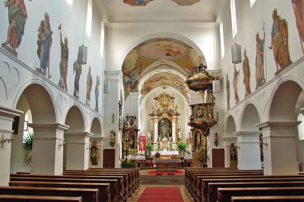 Zwischen Bankreihen mit mehreren Chorgängen, über die Heiligenfiguren gemalt sind, führt der Mittelgang an der Kanzel vorbei zum Hauptaltar und den Seitenaltären, die sich unter einer bemalten Gewölbedecke befinden.