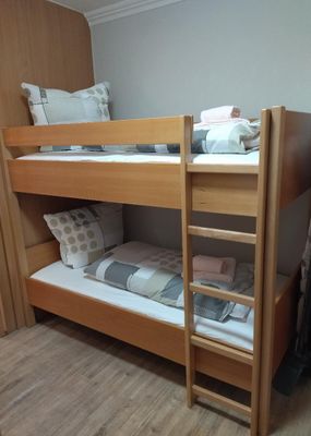 Im Raum mit holzfarbenem Laminatboden steht ein Stockbett. Die Bettbezüge sind grau gemustert, auf den Betten liegen Hand- und Badetücher.