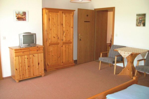 Doppelzimmer mit Kieferholzmöbeln, Sitzecke, Teppichboden und kleinem TV.