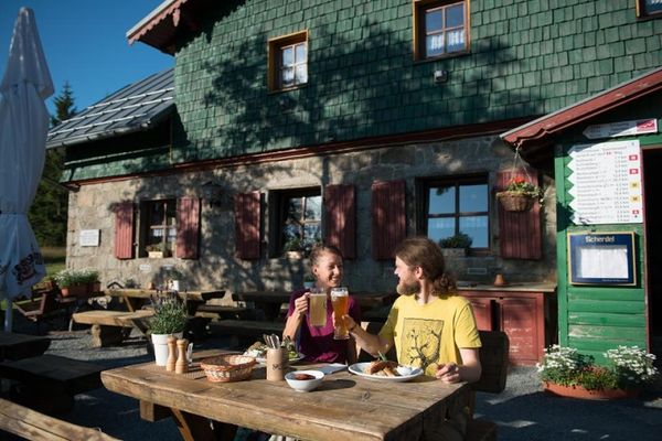 Auf dem Bild sind zwei Personen an einem Tisch vor dem Gasthaus zu sehen.