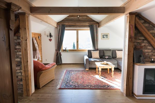 Loft-Wohnraum mit freigelegten, antiken Balken und Mauersteinen, Panoramafenster mit bodenlängen Vorhängen und Alkovenbett.