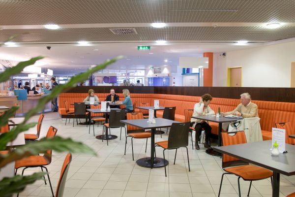 Personen sitzen auf orangefarbenen Bänken an Tischen