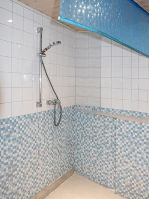 Geflieste Dusche mit Duschkopf, Wandfliesen und Ablage.