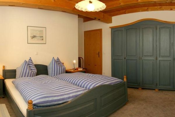 Schlafzimmer mit Doppelbett, großem Kleiderschrank und zwei Nachtkästchen. Die massiven Holzmöbel sind dunkelgrün gestrichen.
