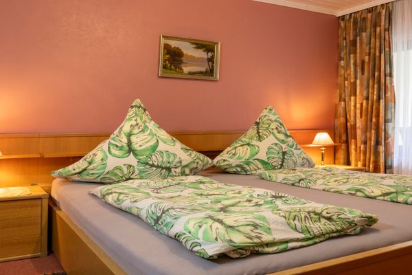 Doppelbett mit gemusterter Bettwäsche, zwei Nachttischen mit Lampen und Fenster mit Vorhängen