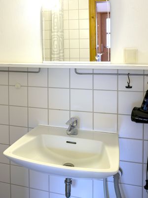 Waschbecken mit Spiegel, Wasserhahn und Fliesenwand im Badezimmer.