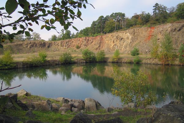 Meterhoch türmt sich Säulenbasalt an der Abbruchkante des Steinbruchs. Davor liegt ein kleiner See.