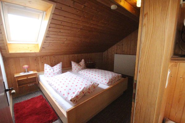 Mansardenzimmer mit Doppelbett, Dachfenster und Teppichboden. Decke und Wände sind holzverkleidet.
