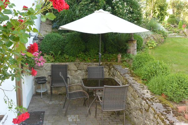 Auf einer ummauerten Terrasse vor dem Eingang zum Untergeschoss befindet sich eine Vierer-Sitzgruppe mit Tisch, Stühlen, Sonnenschirm und Holzkohlengrill. Darüber schön gepflegter Gartenteil.
