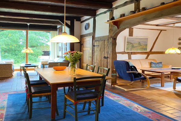 Wohn- und Essraum mit großem Esstisch, Stühlen, Sofa und sichtbaren Holzbalken an Wänden und Decke.