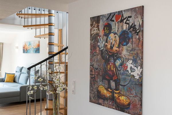 Flur in der Ferienwohnung Bergfeld mit einer weißen Wand auf der sich ein großes Bild befindet; im Hintergrund ist eine Wendeltreppe und eine Couch.