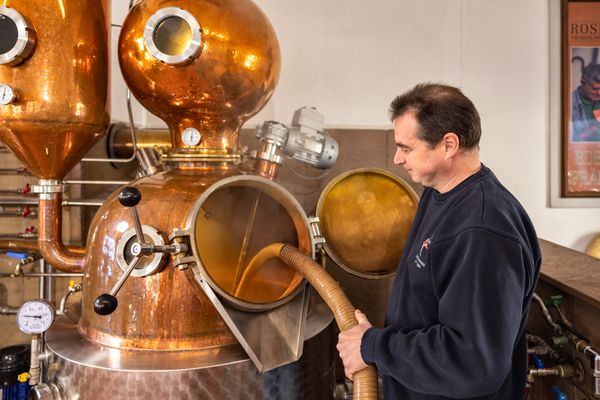 Ein Mann steht an einer Brennanlage und füllt Maische ein.