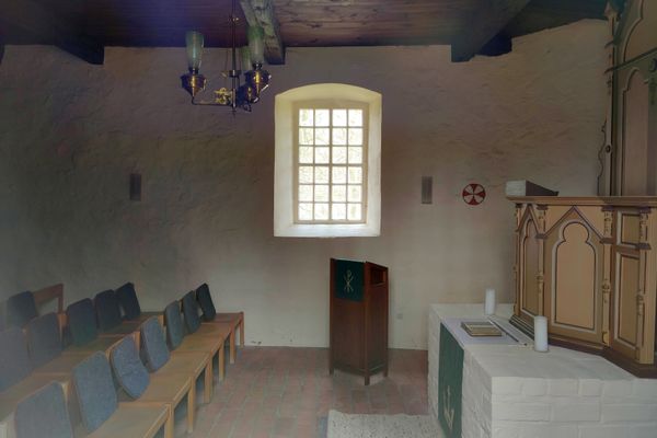 Schlicht gestalteter Altarraum der St. Michaelis-Kapelle in Müssingen mit mehreren Sitzreihen, Altar, Pult, an die Wand gemaltem Weihekreuz und einem Fenster.