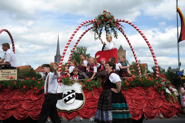 Ein bunt geschmückter Festwagen mit einem Bogenaufsatz, der eine Krone symbolisieren soll. Darunter sitzt die Symbolsfigur der "Slitisia", eingerahmt von Kindern in Trachten. Der Wagen wird flankiert von einem Paar in Tracht.