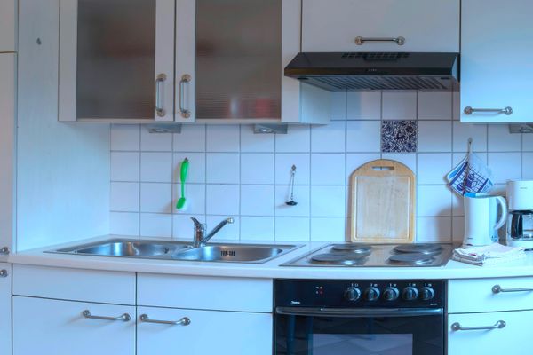 Küchenzeile mit Spüle, Herd und Backofen, darüber Hängeschränke und Dunstabzug.