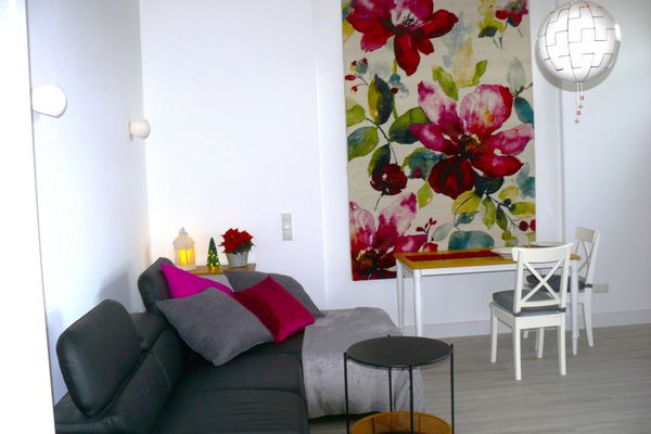 Wohn-Essbereich mit Couch, kleinem weißem Tisch und Blumenbild an der Wand