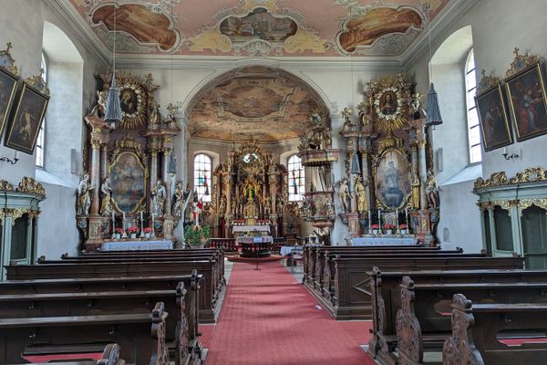Das Bild zeigt den Innenraum der Wallfahrtskirche Mariä Geburt in Glosberg. Man sieht Sitzbänke und prunkvolle Altäre, Gemälde und Statuen.