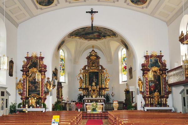 Barocker Kircheninnenraum mit zentralem Hauptaltar, zwei Seitenaltären, Bankreihen, Beichtstühlen und Empore auf der rechten Seite.