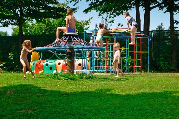 Kinder vergnügen sich an den Spiel- und Klettergeräten, die auf grüner Wiese aufgestellt wurden.