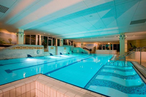 Das Hallenbad "Römerlagune" mit Wasserliegen und beleuchtetem Schwimmbecken. Die Wände sind mit verschiedenen Motiven und Bildern dekoriert.