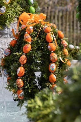 Ostergirlanden in Eierform, an denen Ketten aus orangefarbenen, bemalten Eiern befestigt sind.