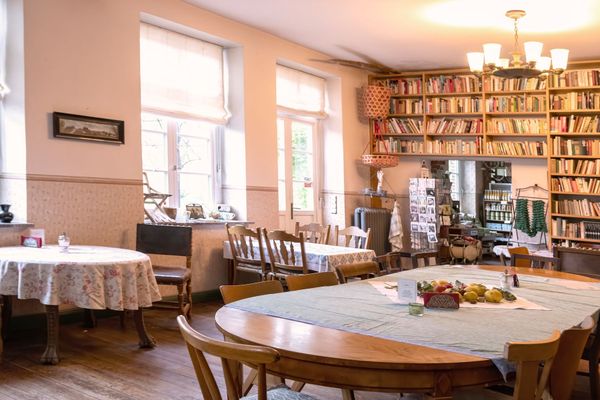 Raum mit mehreren Tischen und Stühlen, großem Bücherregal und Fenstern.