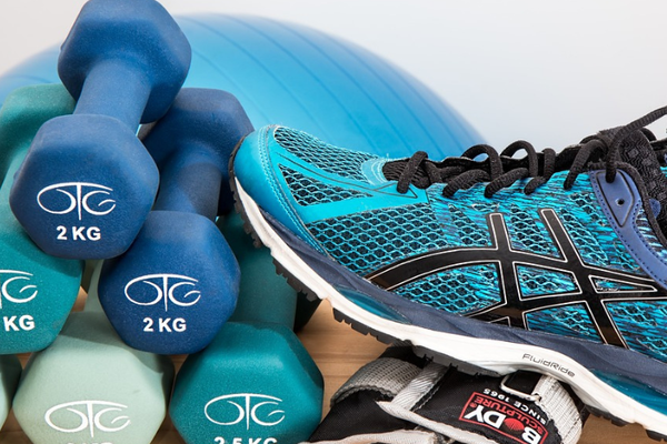 Auf dem Bild ist ein blauer Sportschuh zu sehen, der an einem Stapel von kleinen blauen Hanteln lehnt. Im Hintergrund sieht man einen blauen Gymnastikball.