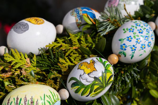 Sechs weiße, kunstvoll mit Blumen und Vogelmotiven bemalte Ostereier