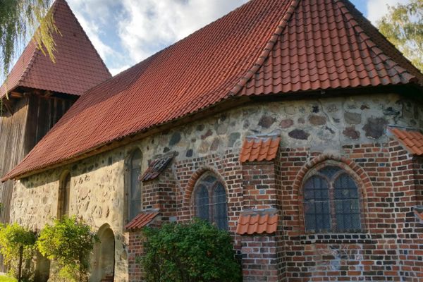 Außenansicht der Alten Kirche Wieren mit Naturstein- und Backsteinmauerwerk sowie dem markanten hölzernen Glockenturm.