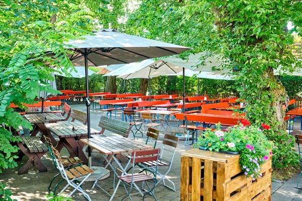 Blick in einen Biergarten mit Bäumen und Tischen und Bänken.