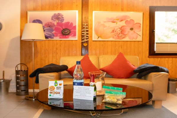 Wohnzimmer mit Sofa und Couchtisch, darauf Flasche, Glas und kleine Gegenstände.