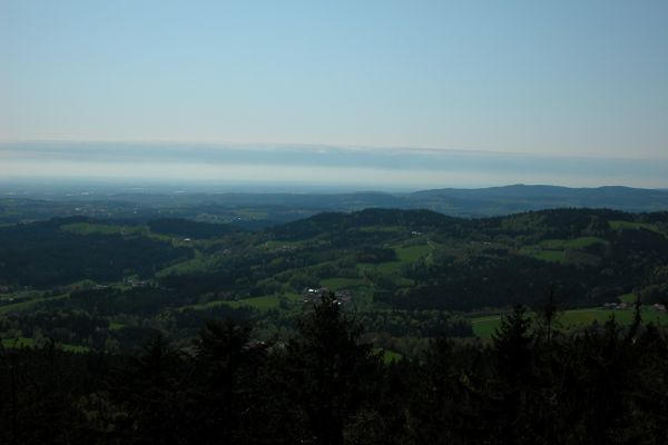 Herrlicher Ausblick über Baumwipfel im Vordergrund hinweg auf eine weite Landschaft mit Wäldern, sanften Hügeln, Wiesen und verstreuten Ortschaften.