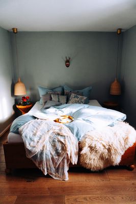 Auf dem Bild ist ein Bett mit vielen Decken in einem Raum mit Holzboden zu sehen.