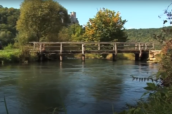 Blick auf einen Fluss über den eine hölzerne Brücke führt.