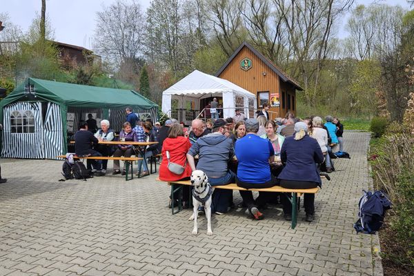 Das Bild zeigt den Hof der Wanderhütte Wartenfels. Es sind voll besetzte Biertischgarnituren sowie zwei kleinere Zelte zu sehen, im Hintergrund die hölzerne Hütte.