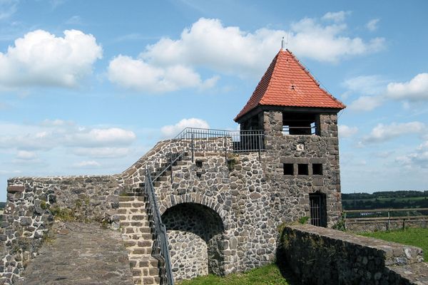 Die aus grauen Basaltsteinen gebaute Burgruine auf dem Schlossberg in Hessens höchstgelegener Stadt Ulrichstein hat einen kleinen Turm mit einem rot eingedeckten Dach. Von der Burg stehen nur die geschliffenen Grundmauern. Zum Burgfried empor führt eine steinerne Treppe mit Metallgeländer.