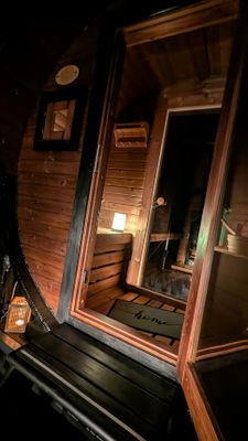Auf dem Bild ist der Eingangsbereich mit Zwischenraum der Fass-Sauna bei Dunkelheit zu sehen.